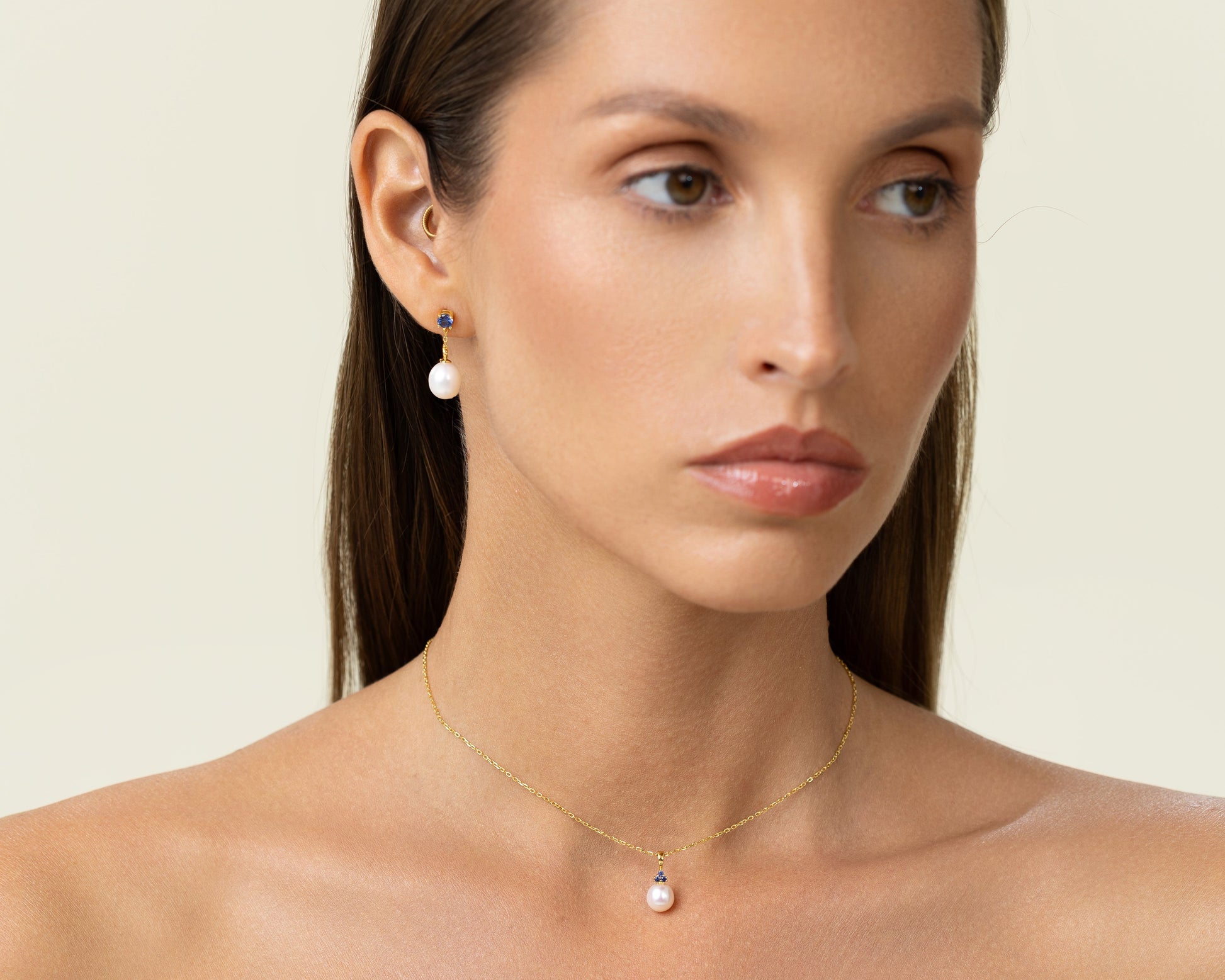 Drop earring featuring a round lab-grown emerald stud and an oval freshwater pearl on 18k gold-plated 925 silver. With trinity sapphire pendant