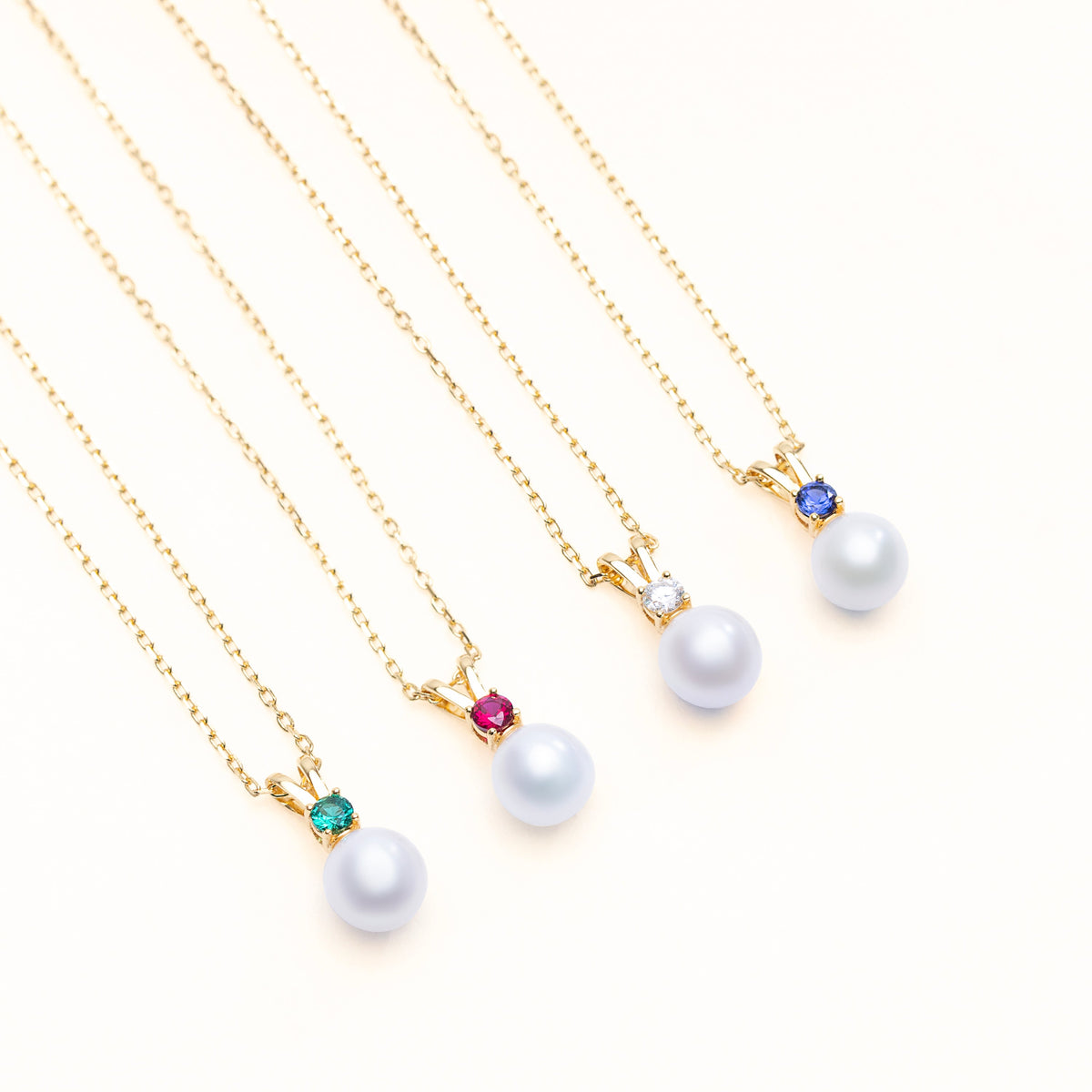 Four Halo freshwater pearl pendants set with lab-grown emerald, ruby, diamond, and sapphire birthstones in 18k gold-plated sterling silver