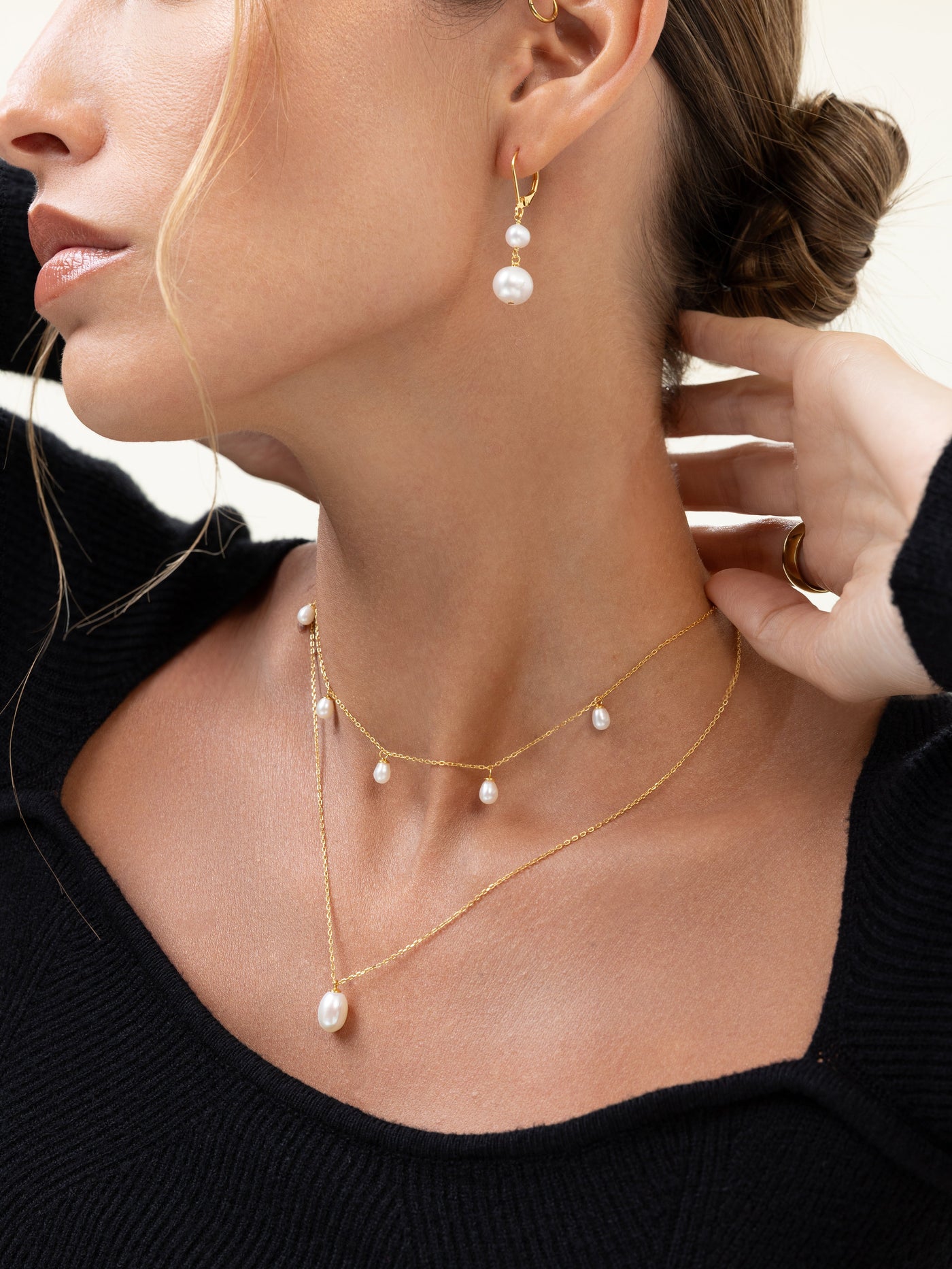 Woman in a black knit top wearing two layered gold freshwater pearl necklaces and pearl drop earrings