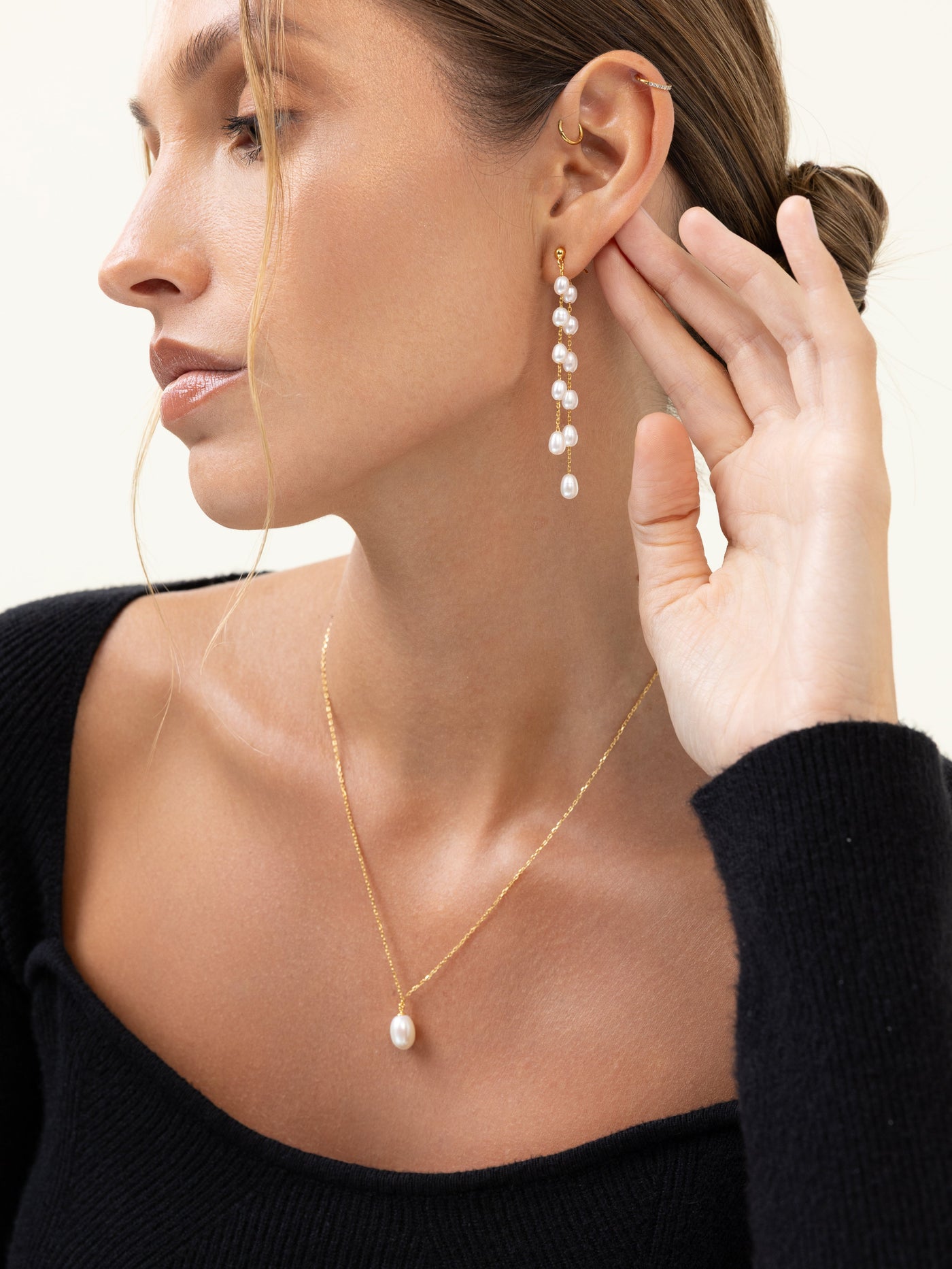 Model wearing linear freshwater pearl drop earrings and a single pearl pendant on a gold chain with a black off-the-shoulder top