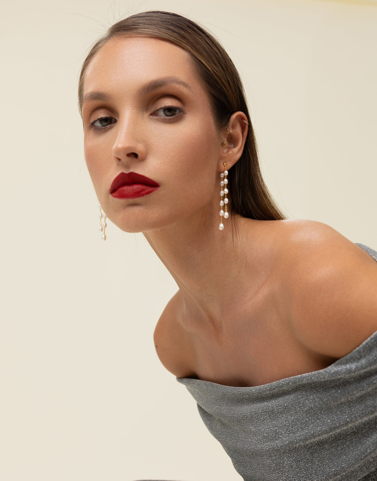 Model in a silver metallic off-shoulder top wearing long gold and freshwater pearl drop earrings